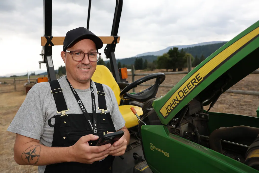 Chris Stoddard, the builder of PyxRanch, beside a tractor, holding a phone and smiling